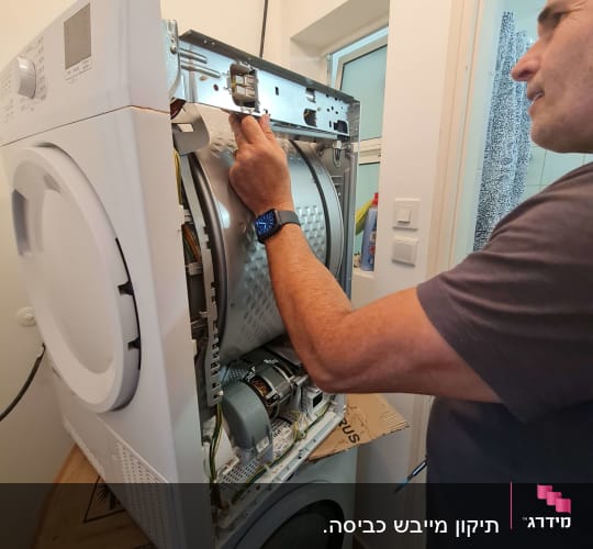 אדם מתקן מכונת כביסה פתוחה בחדר כביסה